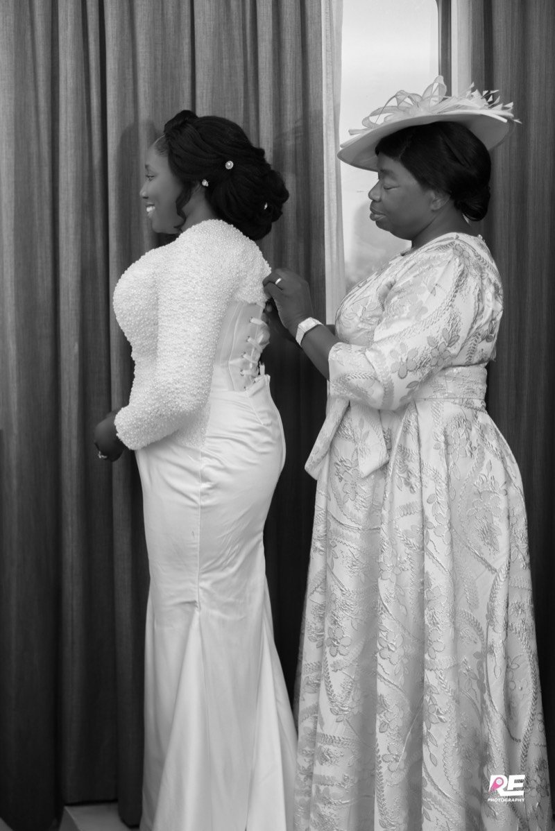 La mère de la mariée lace sa robe, en noir et blanc