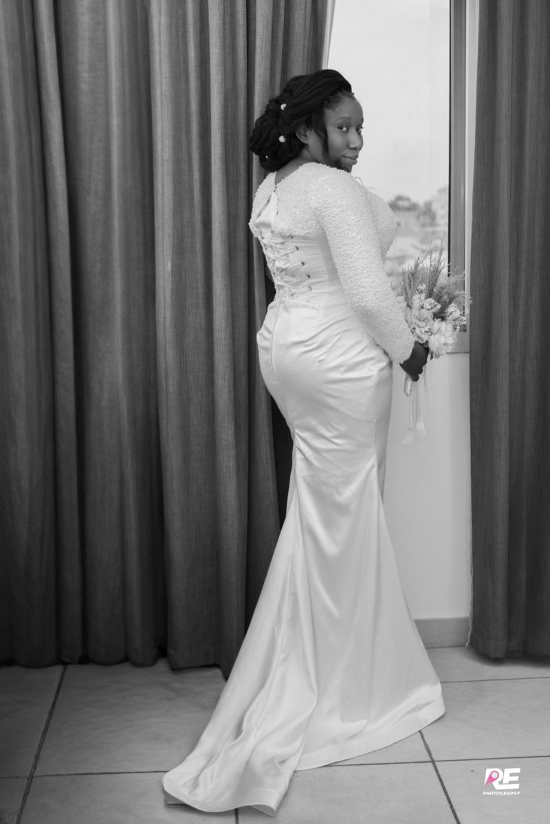 La mariée, de dos, devant la fenêtre, en noir et blanc