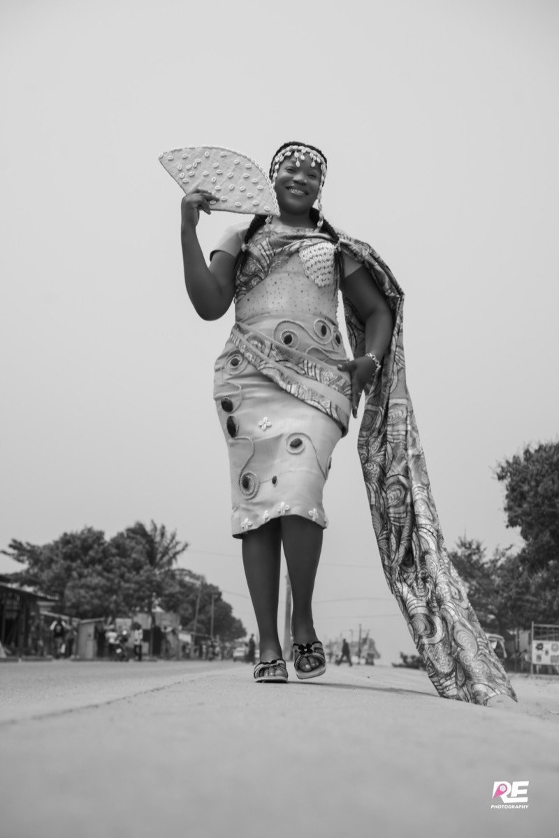 Femme en tenue traditionnelle ornée de cauris, éventail à la main, en noir et blanc